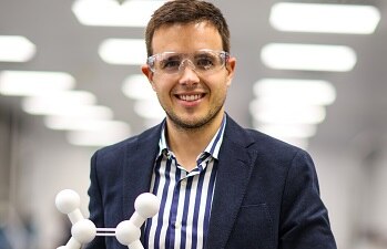smiling employee wearing safety glasses holds a chemical model